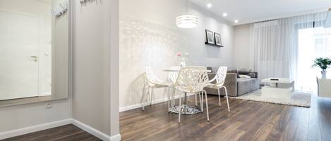 Una sala de estar moderna con comedor, piso de madera, muebles blancos y un espejo grande.