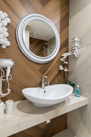 A bathroom with a wooden wall, a round mirror, a white sink, a hairdryer, and a bottle of hand soap.