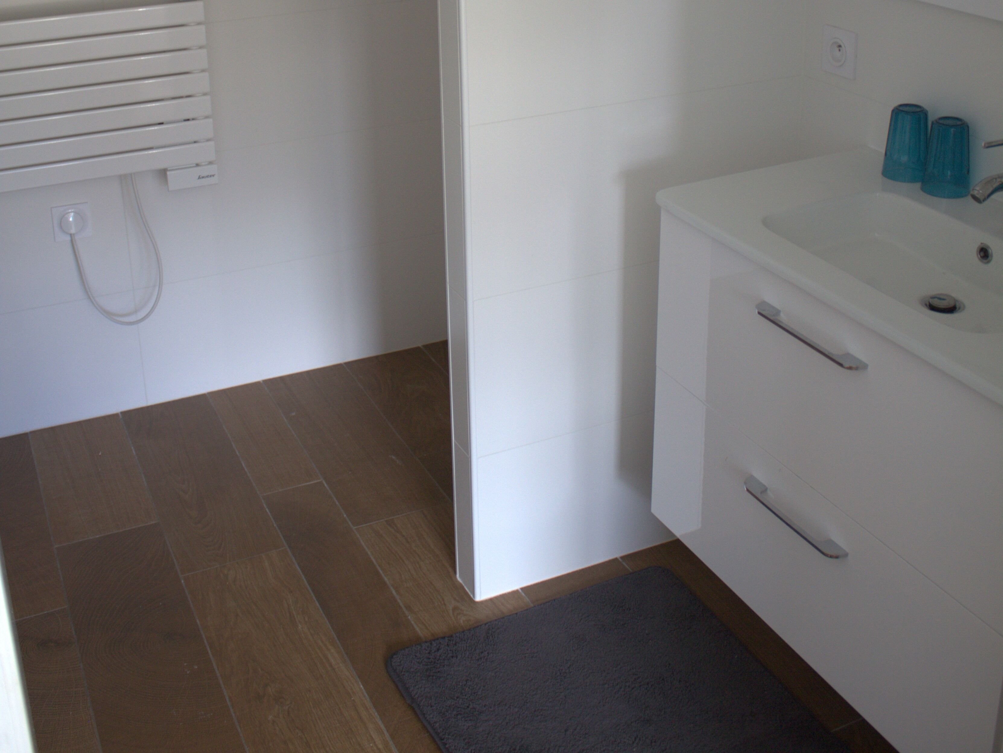 A bathroom with a white sink, two blue glass containers, a white towel rack, and a wooden floor.