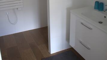 A bathroom with a white sink, two blue glass containers, a white towel rack, and a wooden floor.