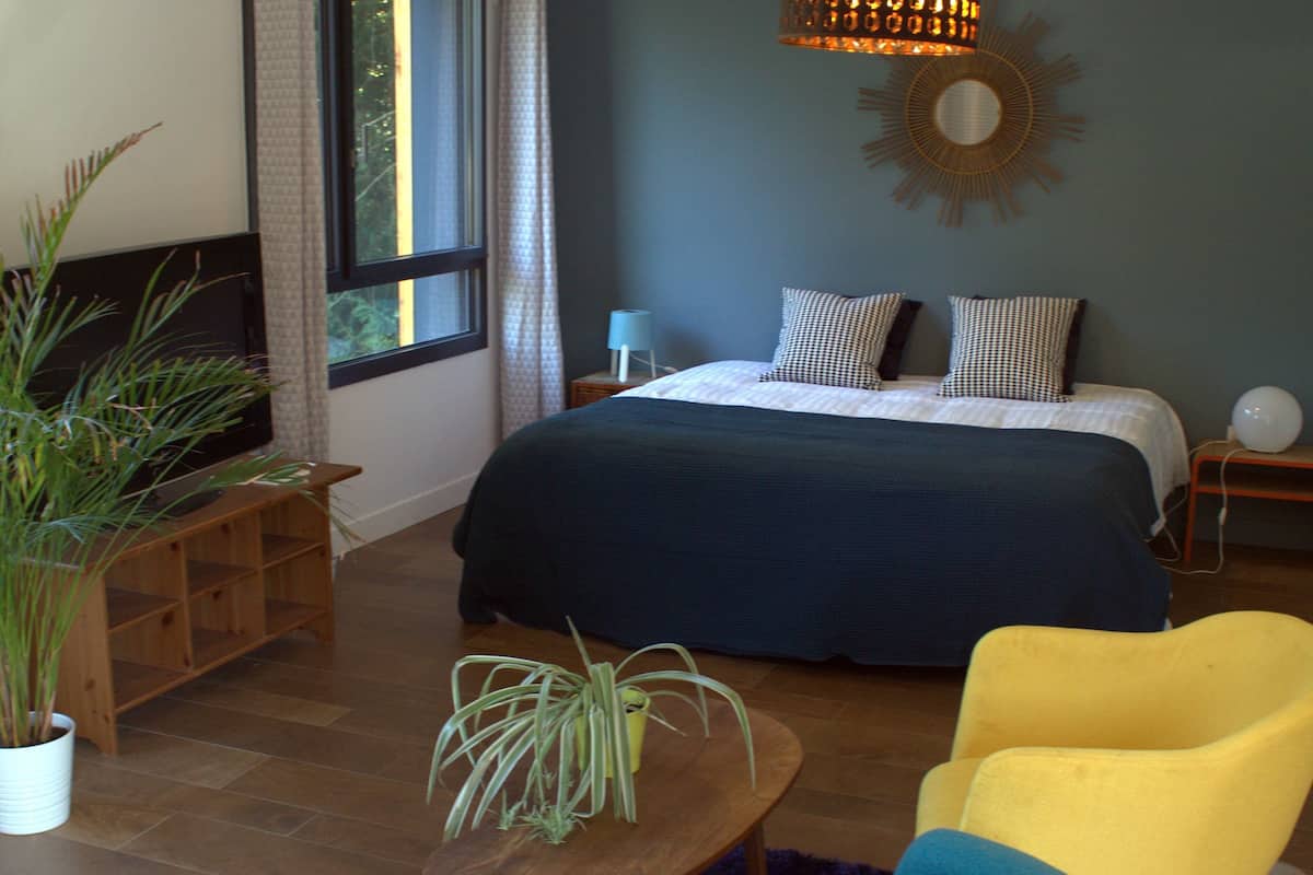 A bedroom with a bed, bedside table, lamp, and a potted plant.