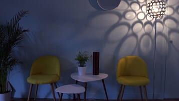 A room with two yellow chairs, a small white table, a potted plant, and a floor lamp casting patterned shadows on the wall.