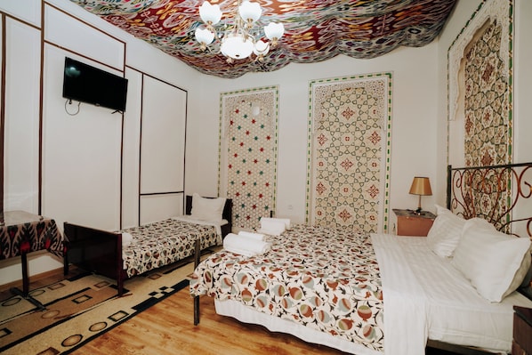 A hotel room with a bed, a smaller bed, a TV, a patterned wall, and a chandelier.