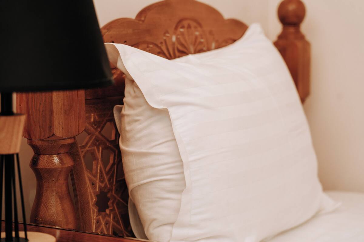 Uma cama com cabeceira de madeira e almofadas brancas.