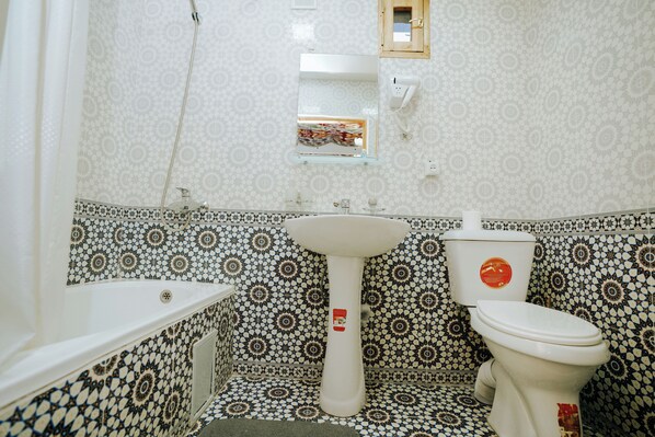 A bathroom with a white sink, pedestal basin, and toilet, all set against a patterned tile wall.