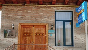 A hotel entrance with a wooden double door, a staircase leading up, and a sign indicating the hotel's name and location. - B-House (Bukhara)