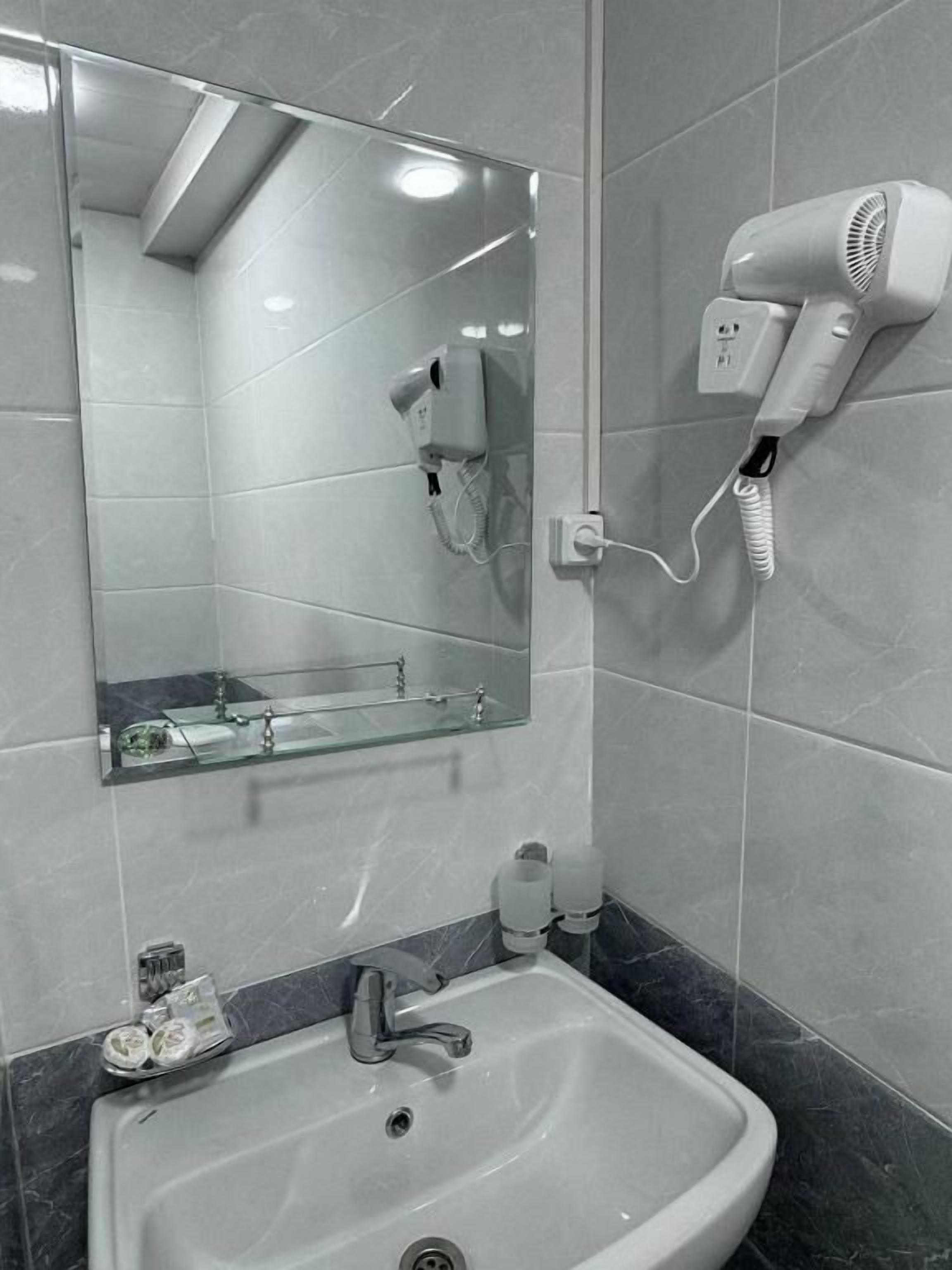 Baño con lavamanos, espejo y secador de pelo montado en la pared.