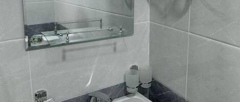Baño con lavamanos, espejo y secador de pelo montado en la pared.