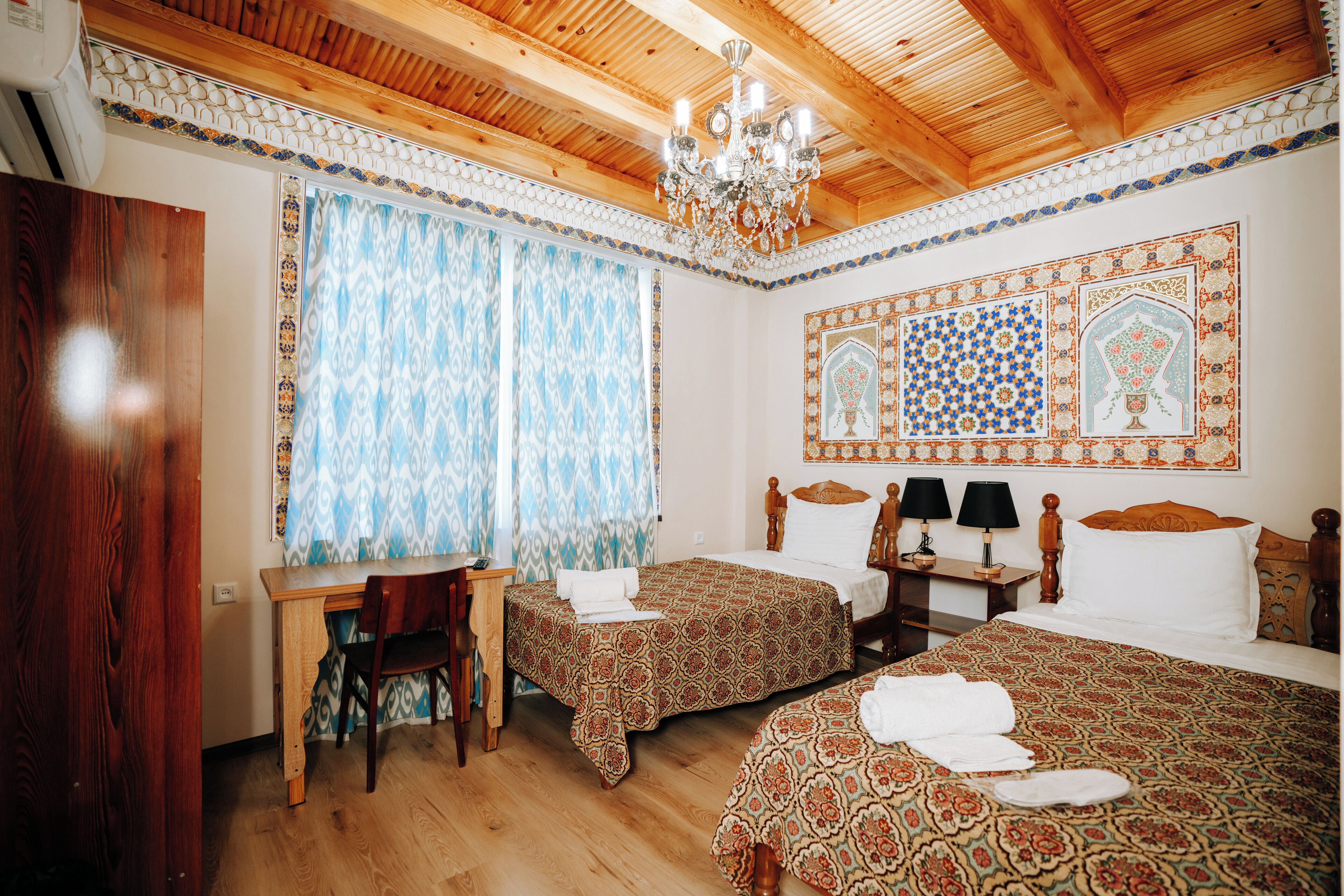 A traditional room with two beds, a desk, and a chandelier.