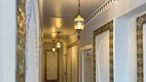 Un pasillo con decoraciones ornamentales en las paredes, suelo de baldosas y lámparas colgantes.