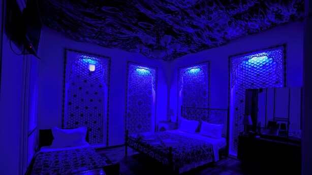 A room with a patterned ceiling, a bed with a patterned bedspread, and a nightstand with a lamp. - B-House (Bukhara)