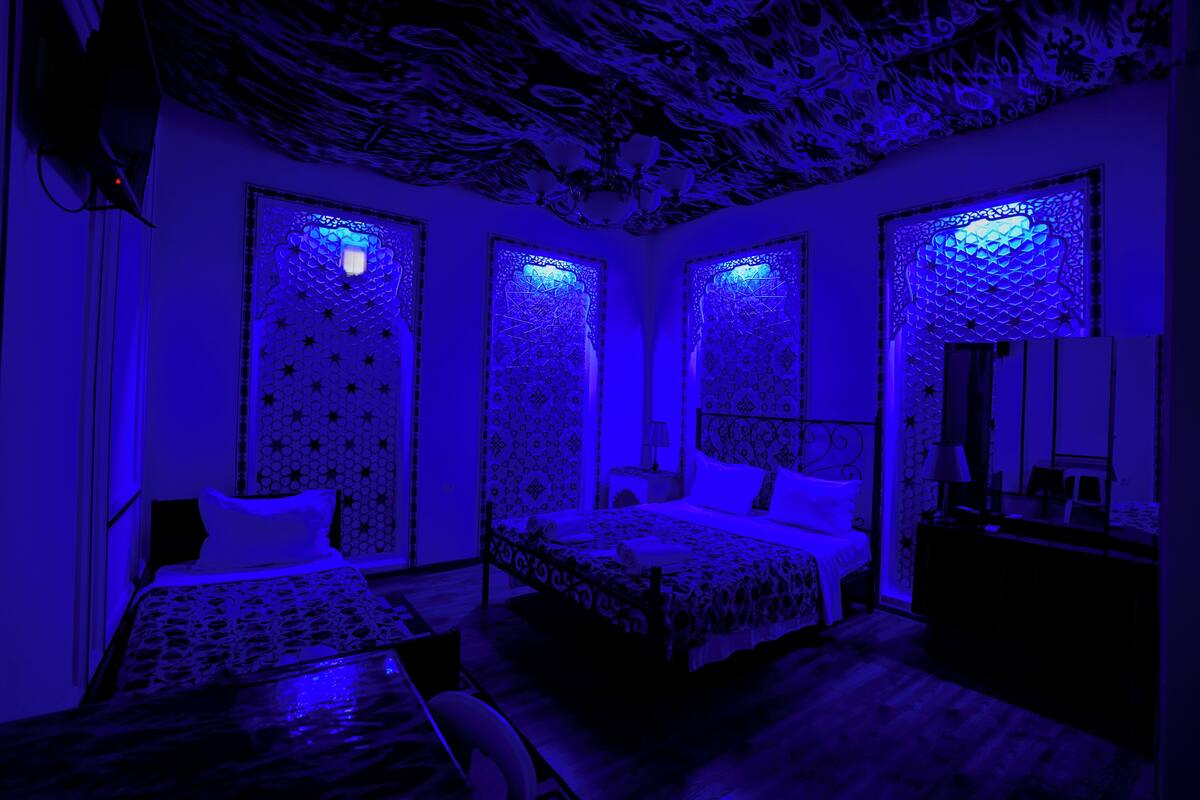 Quarto com teto estampado, cama com colcha estampada e mesa de cabeceira com abajur.