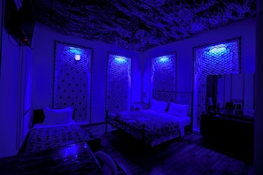 A room with a patterned ceiling, a bed with a patterned bedspread, and a nightstand with a lamp.