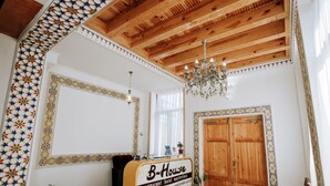 A hotel room with a wooden ceiling, a chandelier, a wooden door, and a sign that reads "B-House restaurant hotel masterclass." - B-House (Bukhara)