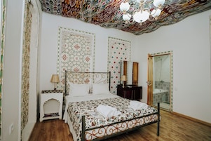 Un dormitorio con una colcha estampada, una mesita de noche con lámpara y un espejo en la pared.