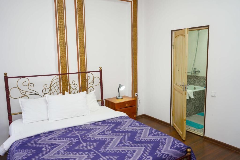 A bedroom with a bed, a nightstand, a mirror, and a bathroom door.