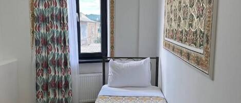 A hotel room with a bed, a window with curtains, a chandelier, and a large patterned wall decoration.
