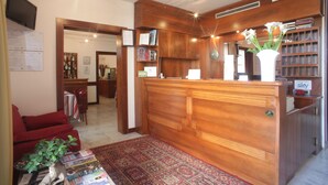 A reception area with a wooden desk, a red sofa, a coffee table with magazines, and a patterned rug. - Albergo Meublé La Corte (Bagnolo San Vito)