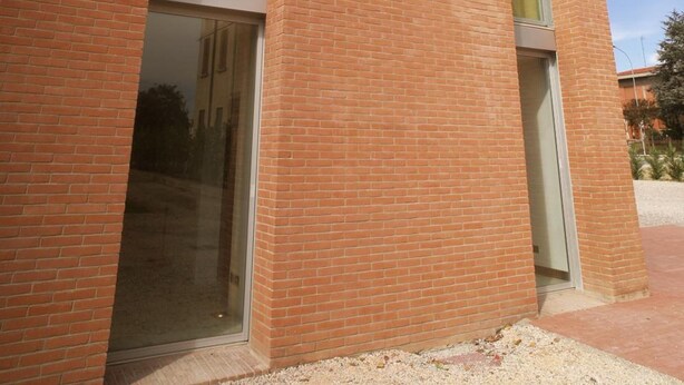 A modern building with a brick facade, large windows, and a clear sky. - Albergo Meublé La Corte (Bagnolo San Vito)
