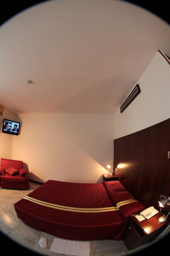 A hotel room with a large bed, a TV mounted on the wall, a bedside table with a lamp, and a red chair. - Albergo Meublé La Corte (Bagnolo San Vito)