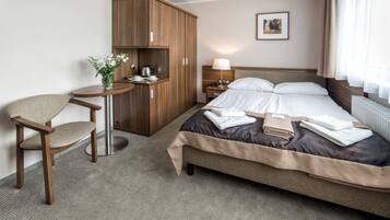 Quarto de hotel com cama, escrivaninha, cadeira, guarda-roupa, mesa de cabeceira com abajur e um quadro na parede.