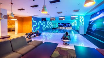 Uma pista de boliche com luzes neon, áreas de estar e diversas pistas de boliche.