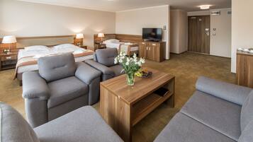 A hotel room with a bed, two sofas, a TV, a wooden cabinet, and a small table with flowers.