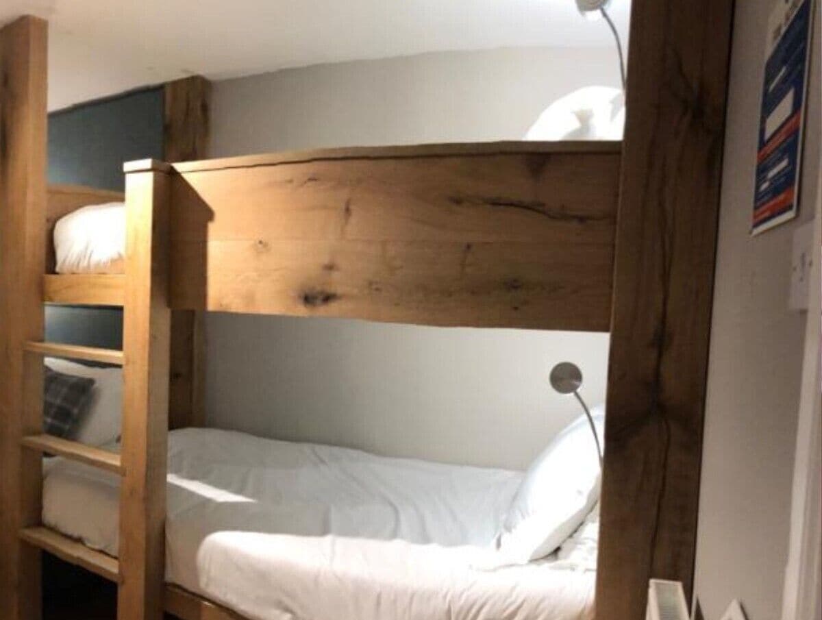 Una cama litera con cabecera de madera y una cama inferior con colchón y almohada blancos.