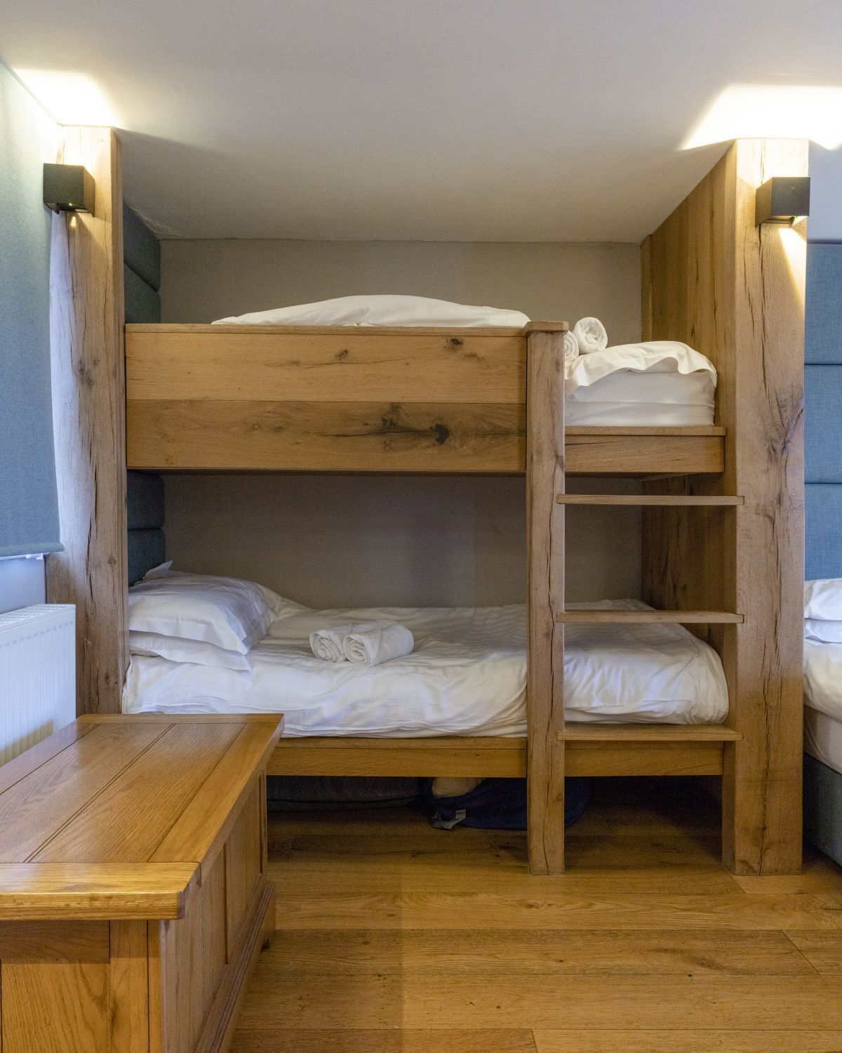 A bunk bed room with a wooden table and a small shelf.