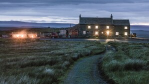 A stone building with multiple windows and a signboard, located in a grassy area with a path leading to it. - The World Famous Tan Hill Inn (Richmond)