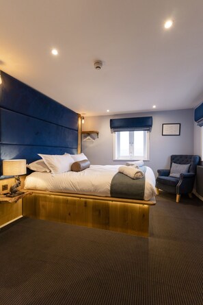 A modern hotel room with a large bed, a wooden headboard, a desk with a lamp, a chair, and a window with a view. - The World Famous Tan Hill Inn (Richmond)