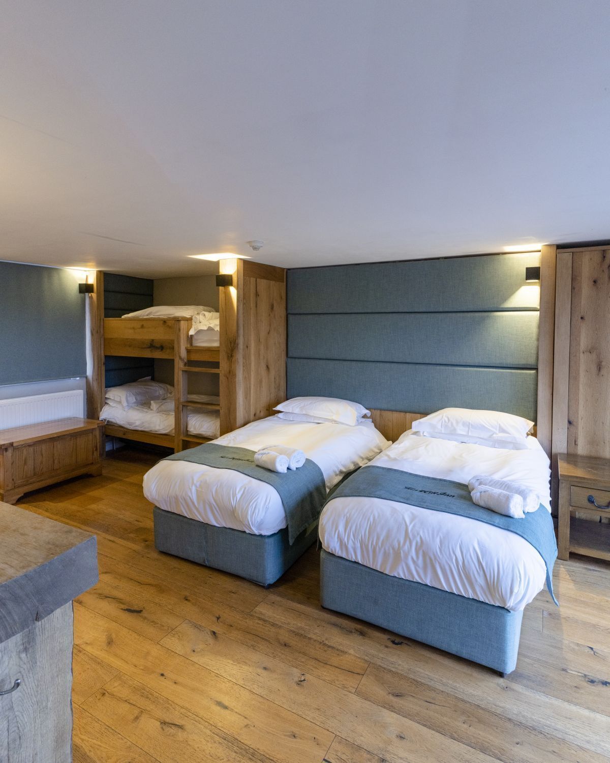Una habitación con dos camas, literas de madera, un banco y una pequeña mesa.