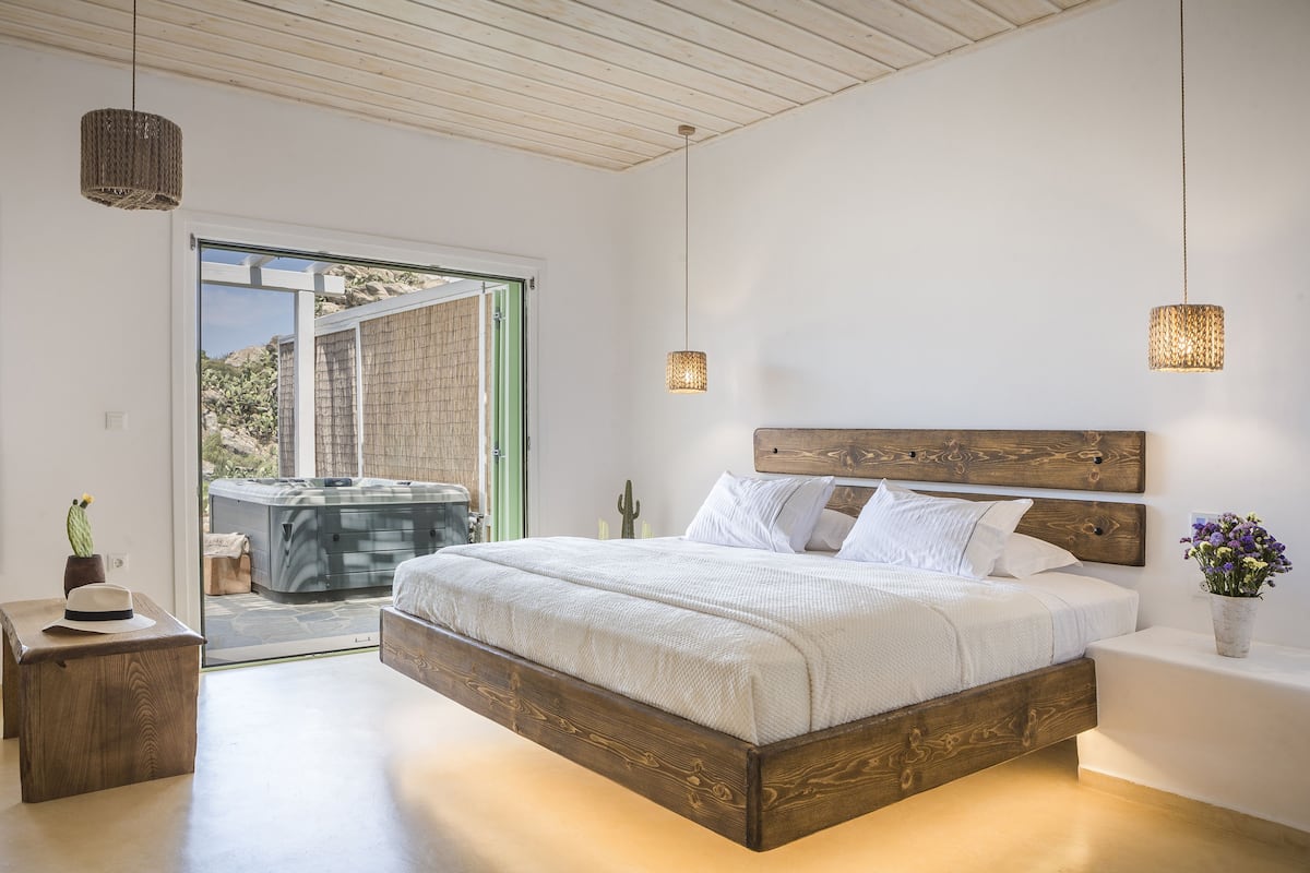 Un dormitorio moderno con una cama de madera, una mesita de noche pequeña, una mesita auxiliar y vistas a un jacuzzi exterior.