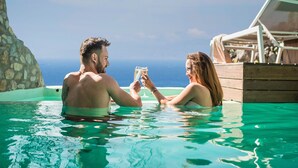 A couple in a clear pool with a wooden deck and lounge chairs, overlooking a body of water. - Klidon Dreamy Living Suites (Mykonos)