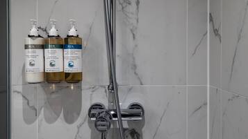 Een badkamer met een marmeren wand, een douche en drie flesjes Ren-producten.