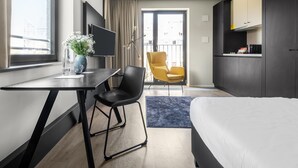 A modern hotel room with a bed, a desk, a chair, a TV, and a kitchenette.