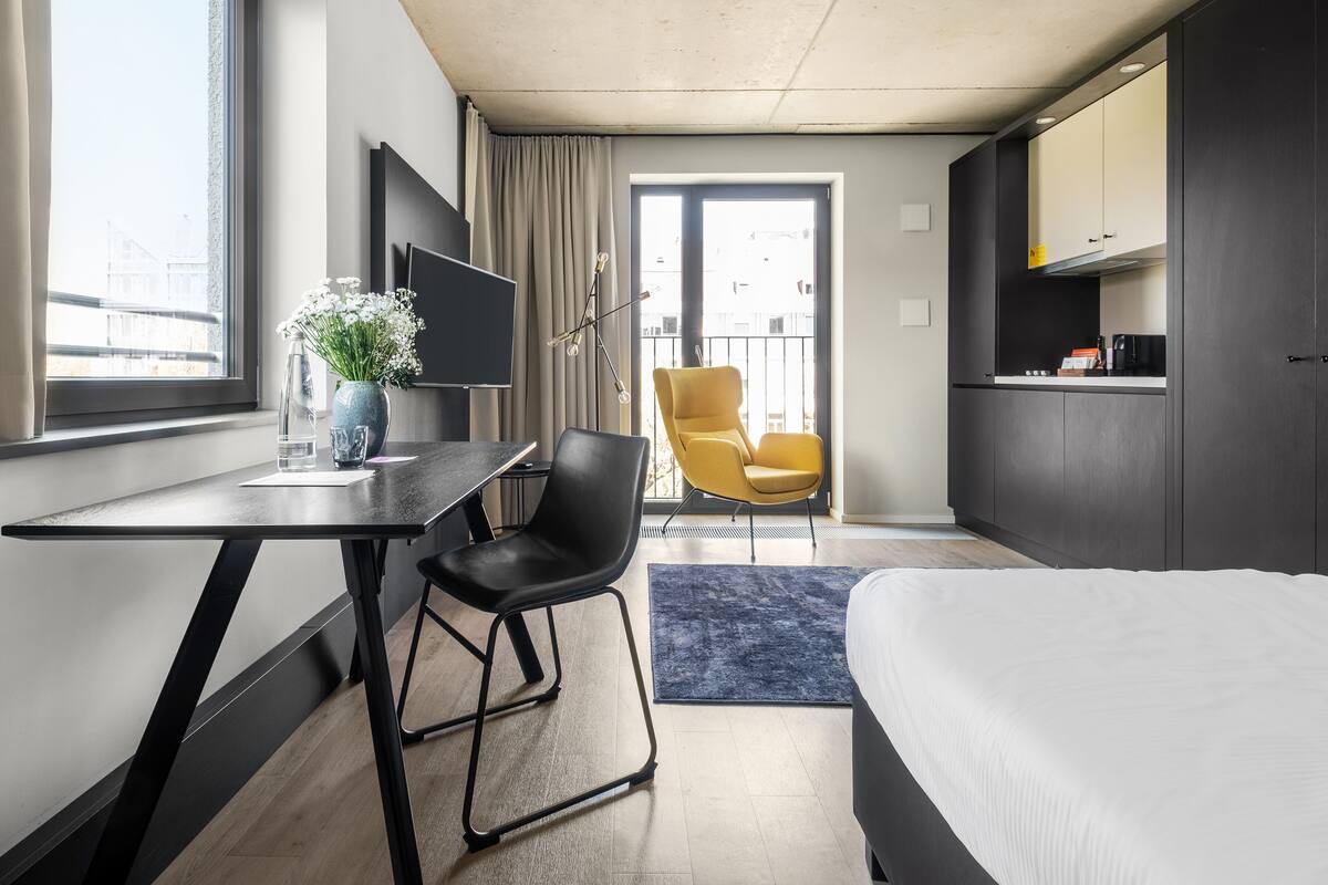 Een moderne hotelkamer met een bed, een bureau, een stoel, een televisie en een kitchenette.