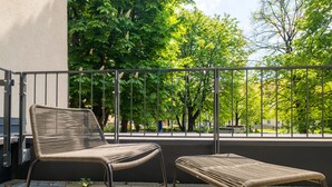 A balcony with a wicker chair and a small table, surrounded by a metal railing.