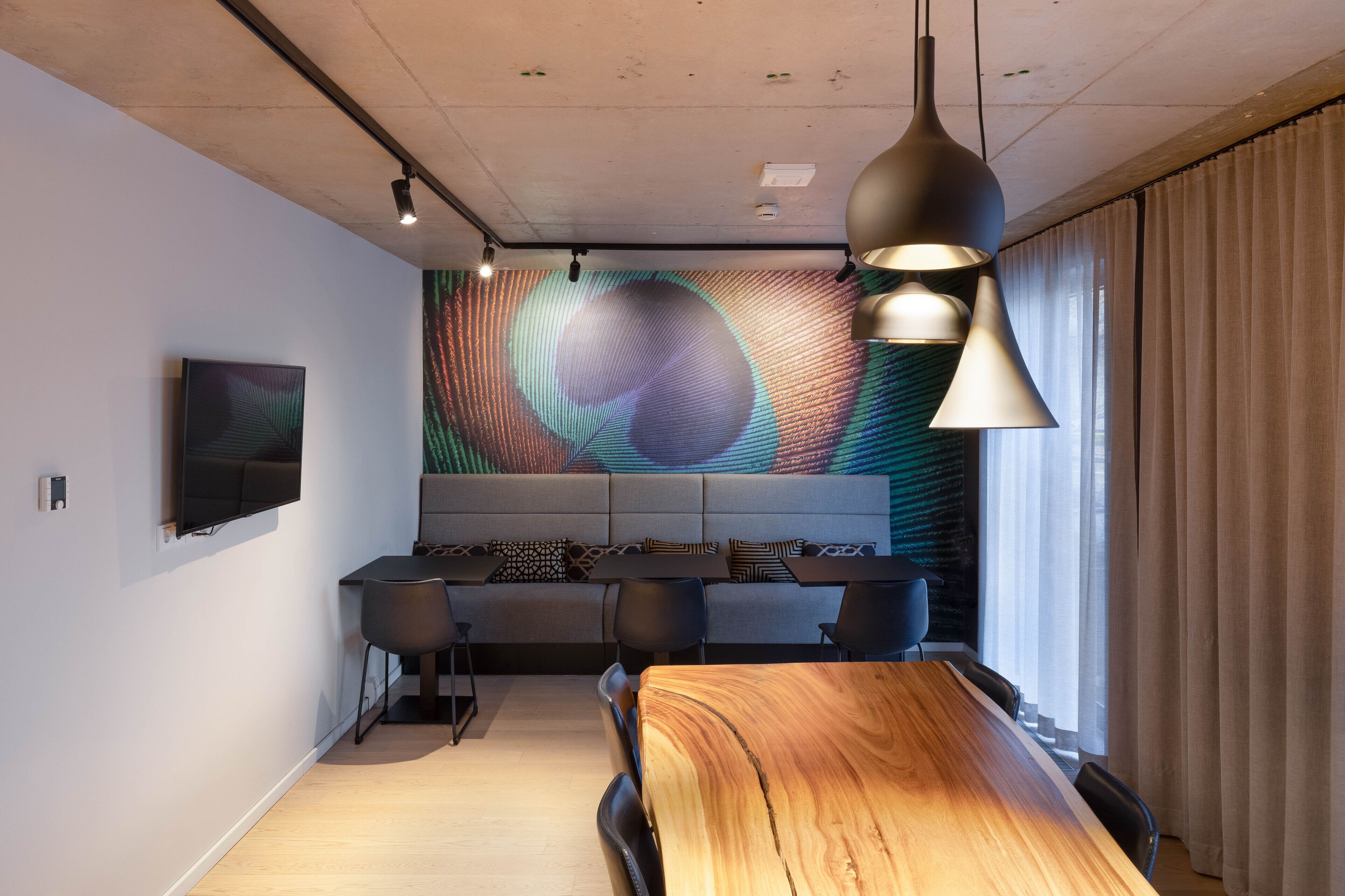 A modern conference room with a long wooden table, black chairs, and a large digital screen on the wall.