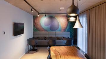 A modern conference room with a long wooden table, black chairs, and a large digital screen on the wall.