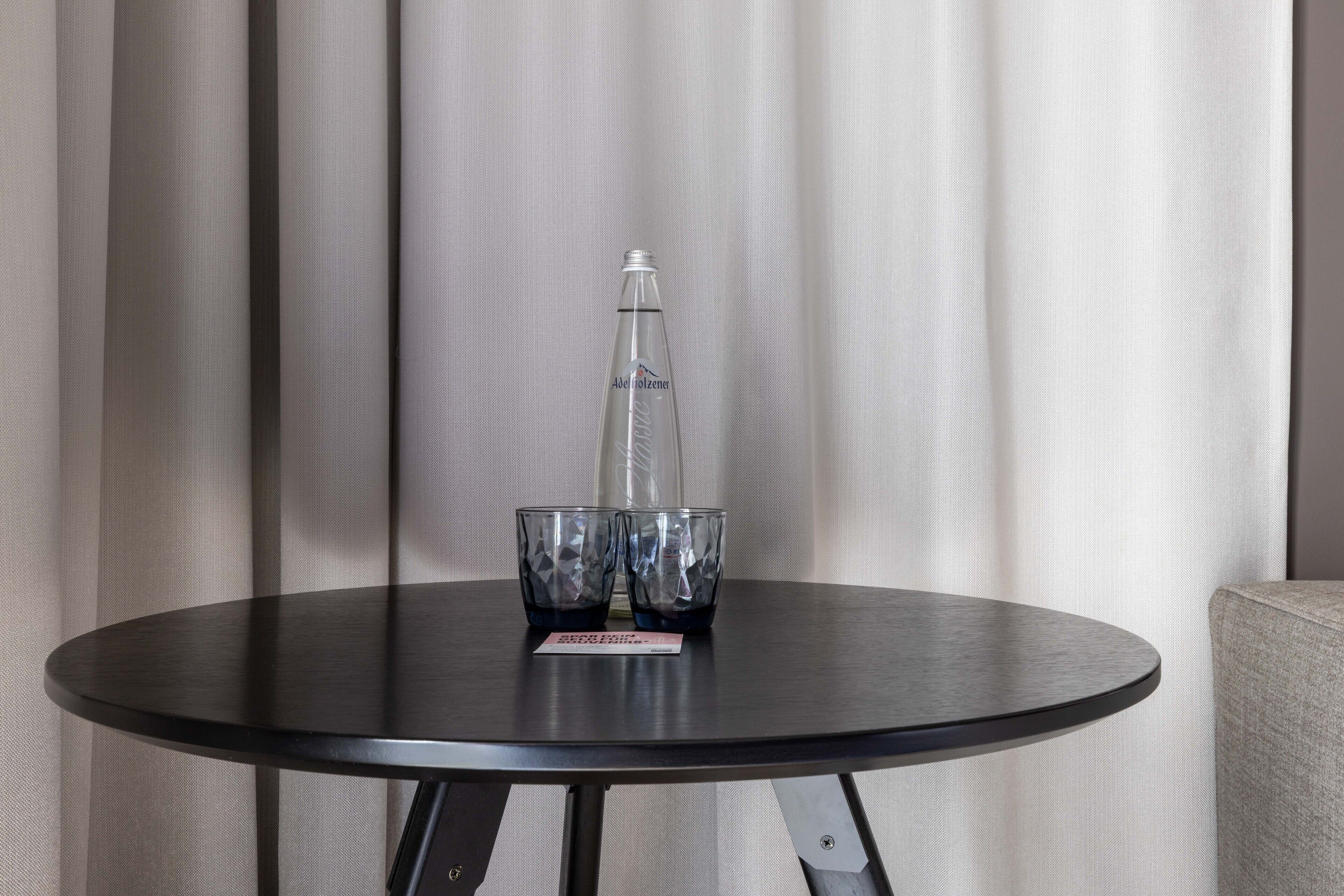 A round table with a bottle and two glasses on it, set against a curtain backdrop.