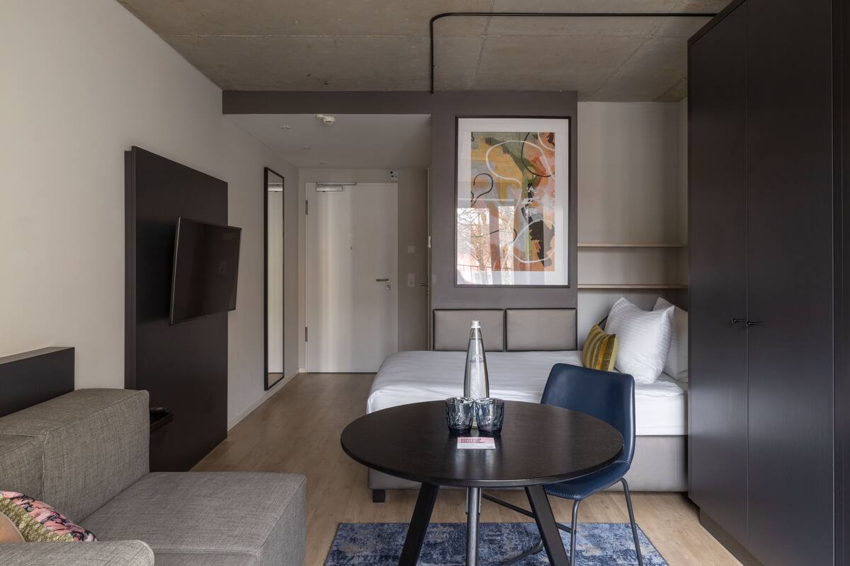 Een moderne hotelkamer met een bed, een bank, een eettafel en een aan de muur bevestigde televisie.