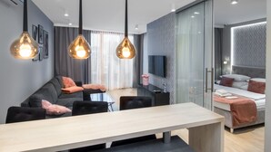 Una habitación de hotel moderna con zona de comedor, sofá, televisor y cama.