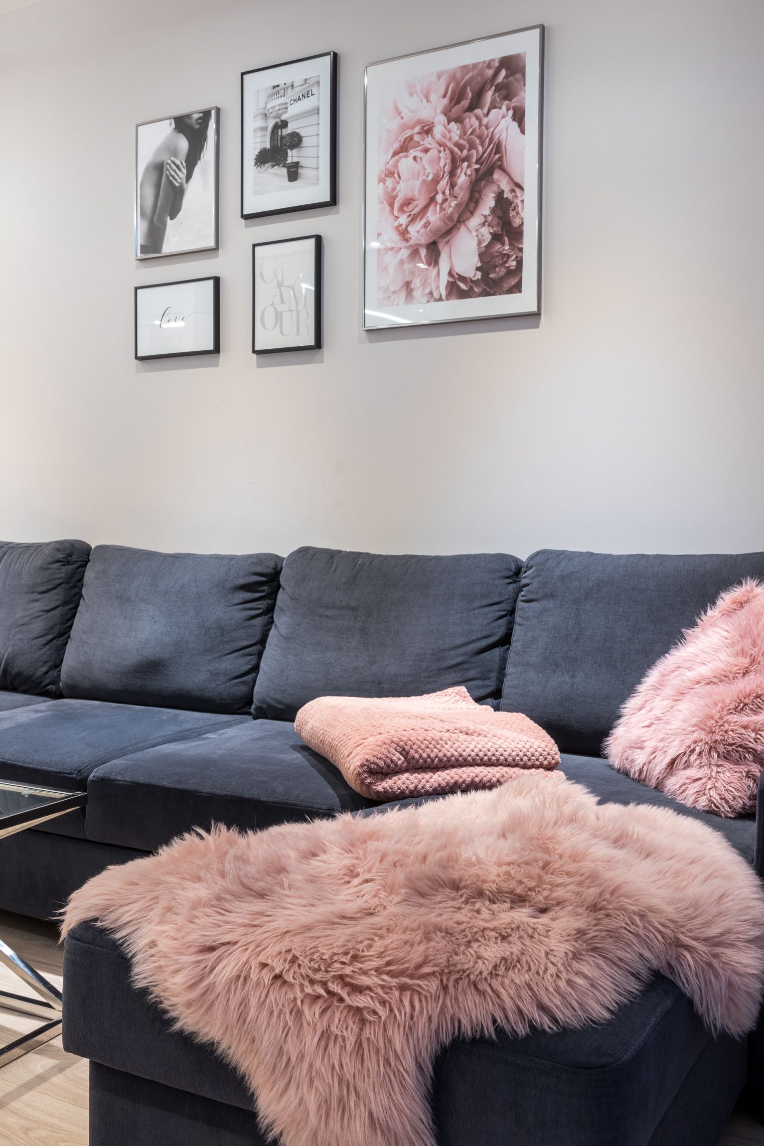 A modern living room with a dark grey sofa, a pink fluffy throw, and framed artwork on the wall.