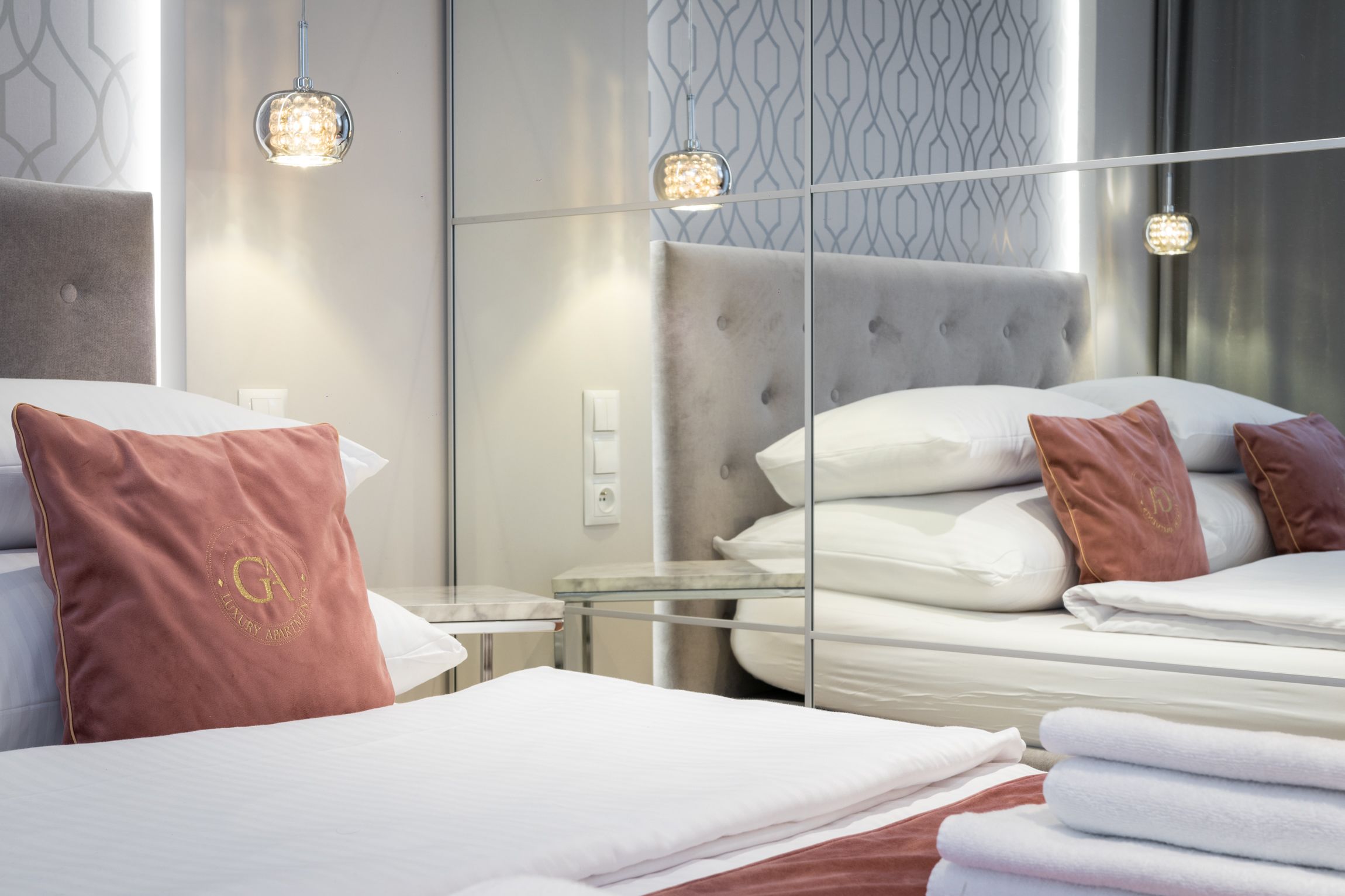 Una habitación de hotel moderna con un espejo grande, un cabecero tapizado y una mesita de vidrio.