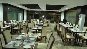 A spacious dining area with multiple tables and chairs, arranged in a modern setting with a tiled floor and glass partitions.