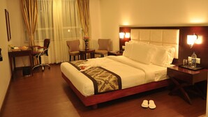 A hotel room with a large bed, bedside tables, a desk, a chair, and a window with curtains.