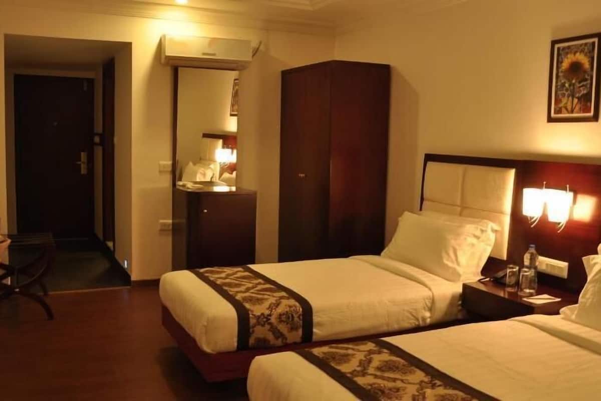 Quarto de hotel com duas camas, mesa de cabeceira com abajur, televisão na parede e um quadro.