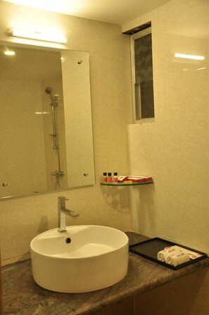 A bathroom with a round sink, a mirror, a shower, and a shelf with toiletries.