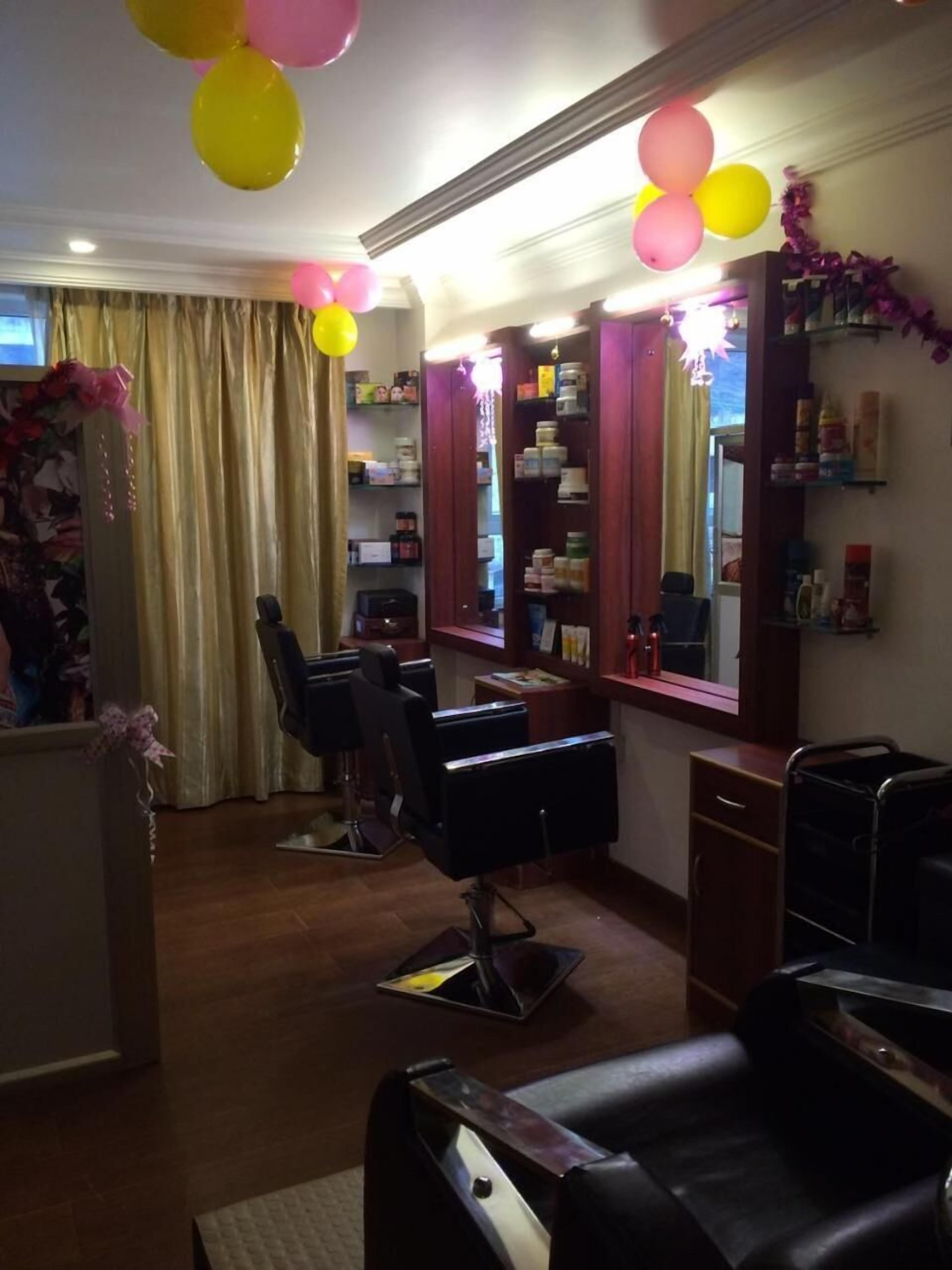 A salon with two black salon chairs, a mirror, shelves with products, and balloons.